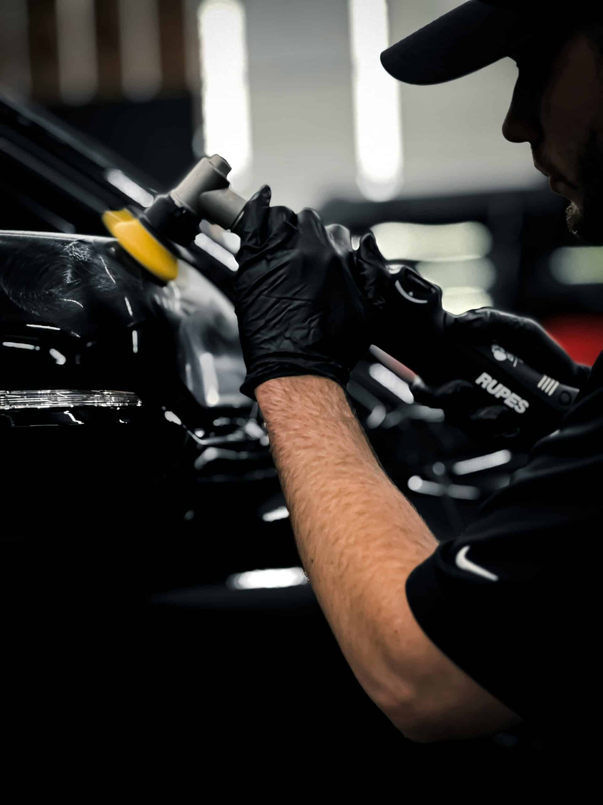 Polissage d'une carrosserie noire avec une polisseuse et un tampon jaune